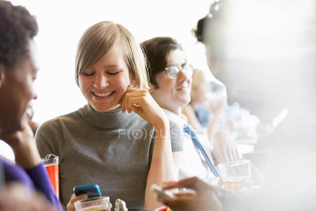 Mujeres revisando teléfonos móviles en reunión con amigos en restaurante . - foto de stock