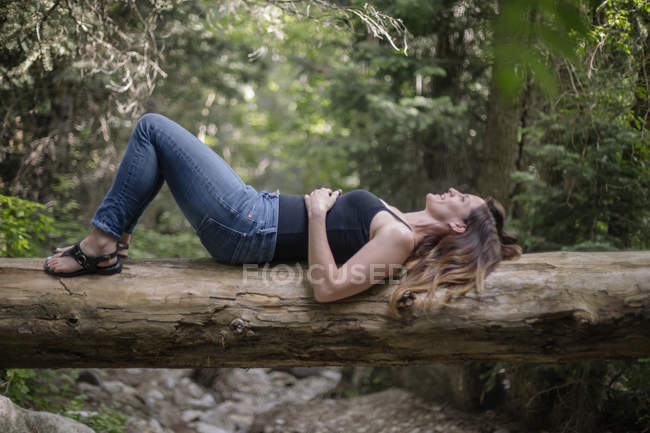 Mulher deitada de costas em tronco de árvore caído na floresta . — Fotografia de Stock
