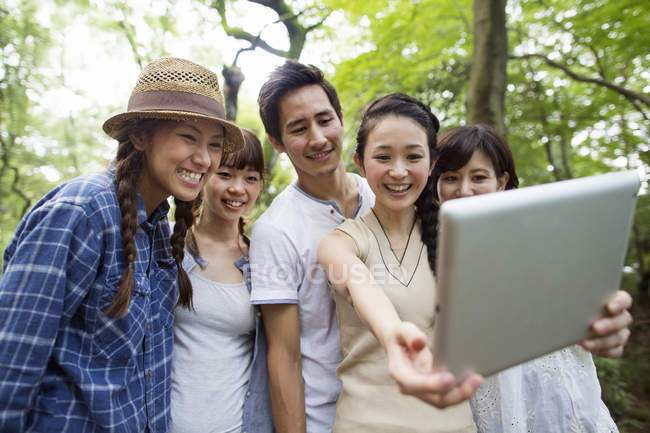 Gruppo di amici asiatici scattare selfie con tablet digitale nella foresta . — Foto stock