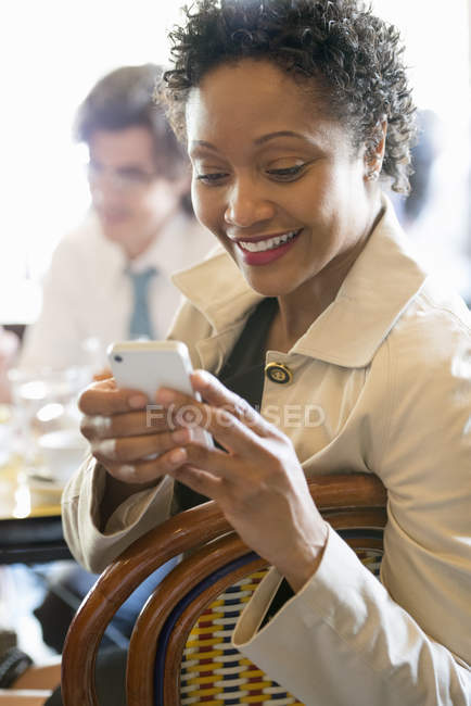 Woman checking smartphone at restaurant table with man in background. — Stock Photo