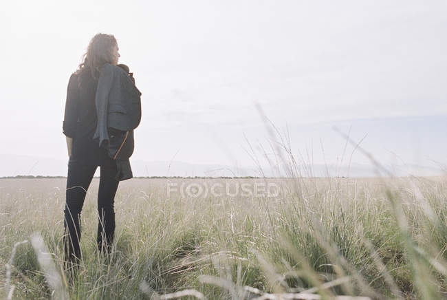 Frau mit Jacke und Rucksack im Grasland stehend, Rückansicht. — Stockfoto