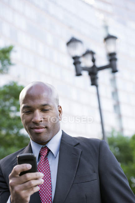 Mid adult man in suit using smartphone in city. — Stock Photo