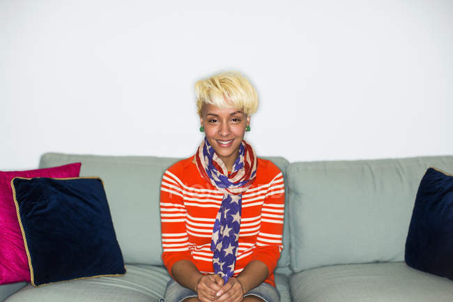 Mujer de raza mixta con el pelo rubio sentado en el sofá y sonriendo
. - foto de stock