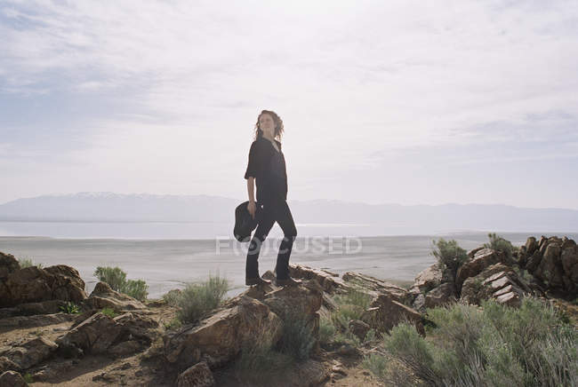 Donna con i capelli castani in piedi su rocce con lago e montagne in lontananza . — Foto stock
