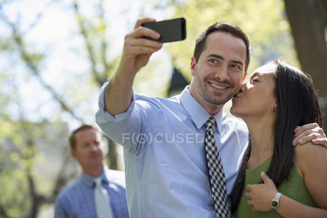 Пара бере селфі зі смартфоном з людиною у фоновому режимі на міській вулиці . — стокове фото