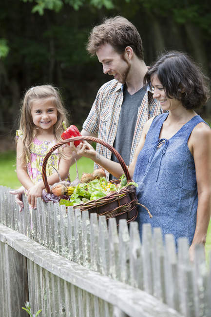 Family standing in garden with basket of vegetables. — Stock Photo