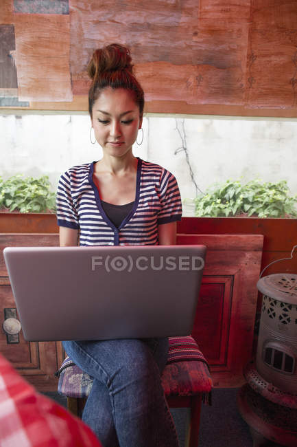 Frontansicht einer Frau, die mit Laptop arbeitet und drinnen auf einem Stuhl sitzt. — Stockfoto