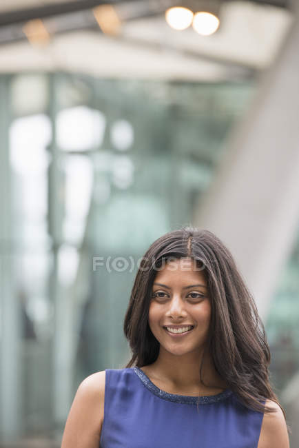 Mujer joven en vestido azul y chaqueta gris de pie en la calle y mirando hacia otro lado . - foto de stock