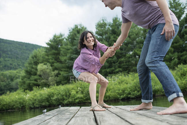 Couple pulling hands on wooden jetty by country lake. — Stock Photo