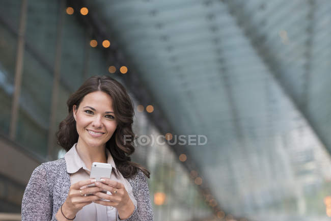 Young businesswoman in grey cardigan using smartphone and smiling. — Stock Photo