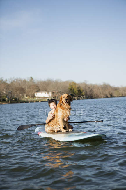 Menina pré-adolescente com cão golden retriever em paddleboard na água . — Fotografia de Stock