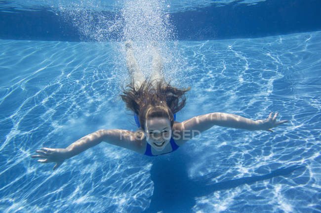 Menina pré-adolescente com fanning cabelo longo nadando debaixo d 'água na piscina . — Fotografia de Stock
