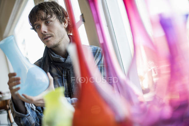 Чоловік тримає блакитну скляну вазу з червоними та рожевими вазами на передньому плані . — стокове фото
