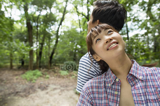 Mujer joven apoyada en el hombro del hombre y mirando hacia arriba en el bosque . - foto de stock