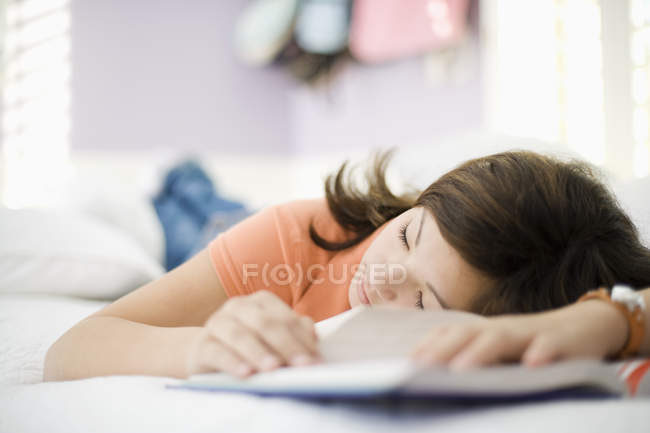 Pre-adolescent girl sleeping on bed with school book. — Stock Photo