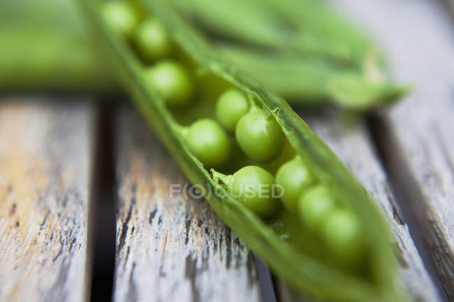 Close-up de ervilhas verdes brilhantes recém-colhidas com vagem aberta na mesa de jardim de madeira — Fotografia de Stock