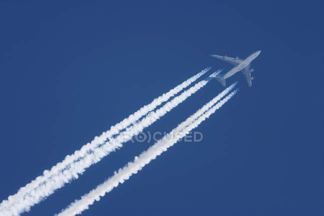 Avion jet en vol avec trajectoires sur ciel bleu . — Photo de stock