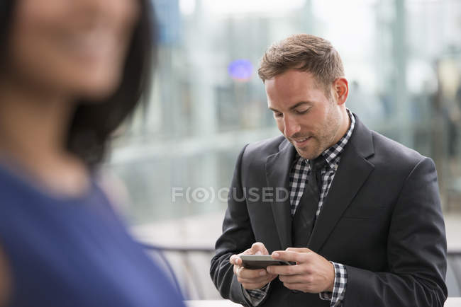 Uomo in giacca e cravatta controllo smartphone con donna in primo piano . — Foto stock