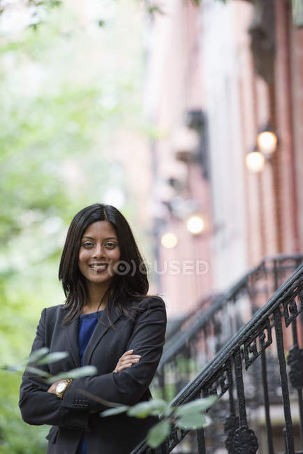 Giovane donna in giacca grigia in piedi su gradini esterni edificio con le braccia incrociate
. — Foto stock