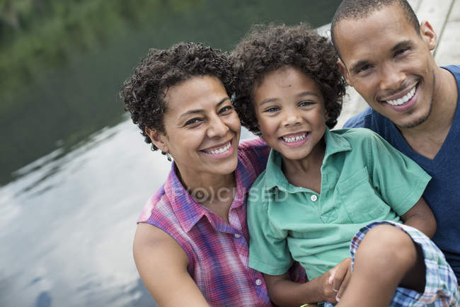 Retrato de pais felizes e menino idade elementar por lago no verão . — Fotografia de Stock