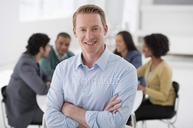 Selbstbewusster Geschäftsmann steht im Besprechungsraum mit Kollegen im Hintergrund. — Stockfoto