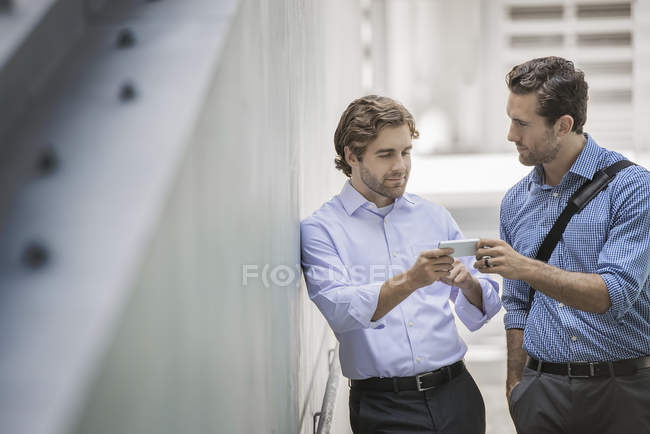 Два бизнесмена стоят на городской улице и делятся смартфоном . — стоковое фото