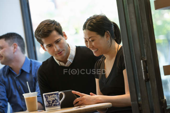 Group of people sitting around  table in coffee shop with drinks and using digital tablet. — Stock Photo