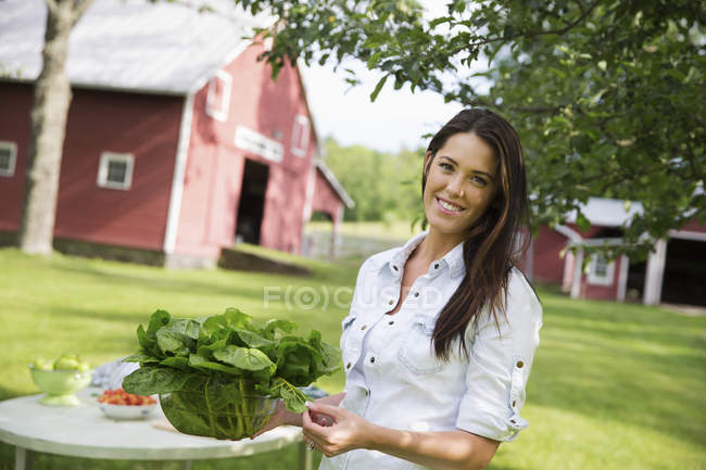 Молода жінка з довгим волоссям несе миску зі свіжих зелених листя салату . — стокове фото