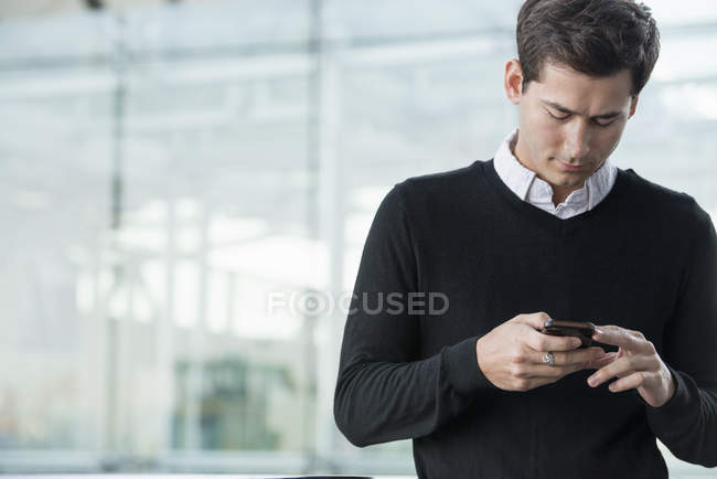 Hombre joven comprobando teléfono inteligente en frente del edificio moderno . - foto de stock