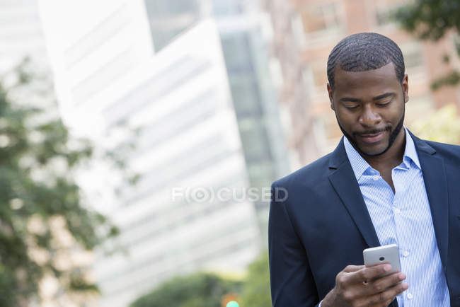 Businessman in blue jacket using smartphone on city street. — Stock Photo