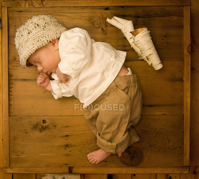 Newborn baby lying asleep on side in wooden box with scroll of white tree bark beside. — Stock Photo