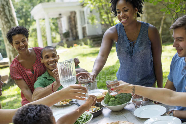 Amigos e familiares se reúnem em torno da mesa de jantar no jardim do campo . — Fotografia de Stock