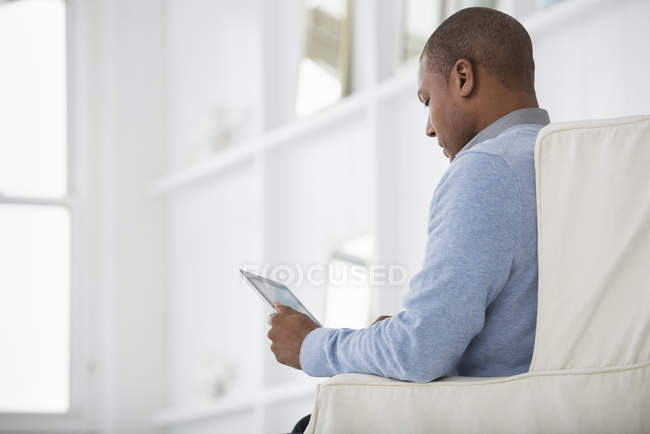 Seitenansicht eines Mannes, der im Sessel sitzt und digitales Tablet nutzt. — Stockfoto