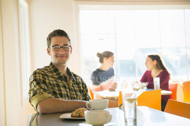 Young man sitting at coffee shop counter with women talking in background. — Stock Photo