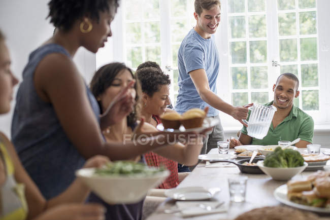 Group of men and women gathering around dining table and sharing meal ...