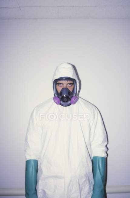 Mann in weißem Schutzanzug, blauen Handschuhen und Atemmaske. — Stockfoto