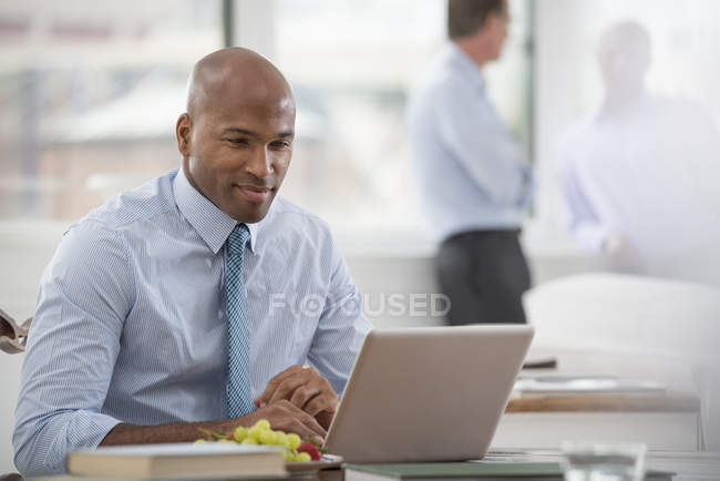 Empresário de camisa e gravata sentado na mesa e usando laptop no escritório . — Fotografia de Stock