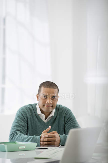 Hombre sentado con las manos apretadas en el escritorio en la oficina
. - foto de stock