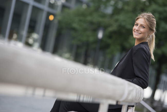 Young businesswoman in black jacket leaning on railing in city. — Stock Photo