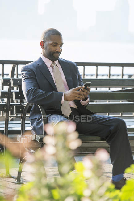Geschäftsmann sitzt auf Stadtbank und checkt Smartphone. — Stockfoto