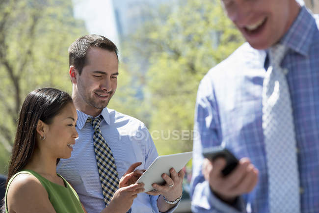 Businessman checking smartphone with couple sharing digital tablet in city park. — Stock Photo