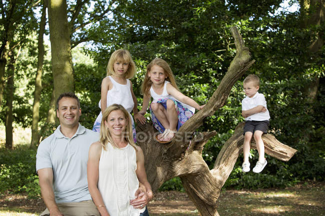 Família com três filhos posando juntos pela árvore no parque . — Fotografia de Stock