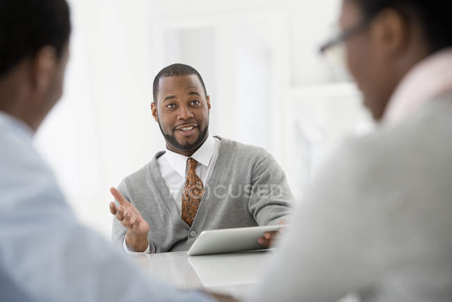 Mid adult man with digital tablet sitting at meeting with couple. — Stock Photo