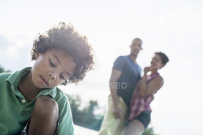 Elementary age boy sitting on sunny lake jetty with parents. — Stock Photo