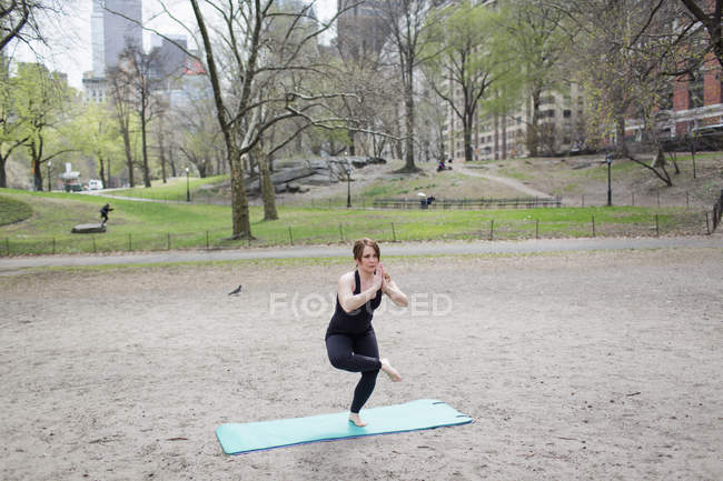 Woman doing yoga on one leg on gym mat in Central Park. — Stock Photo