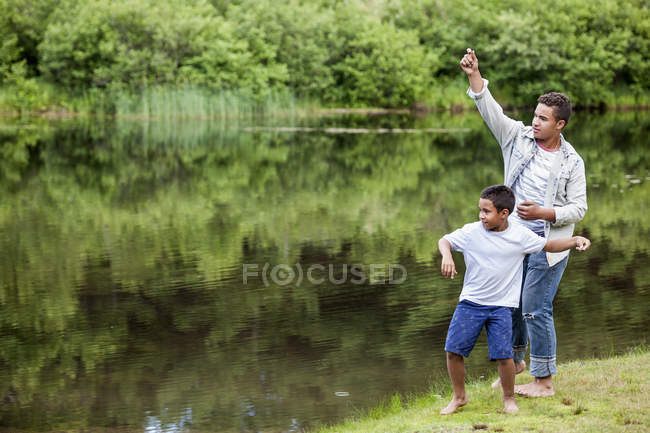 Dois irmãos atirando pedras na água na margem do lago em bosques . — Fotografia de Stock