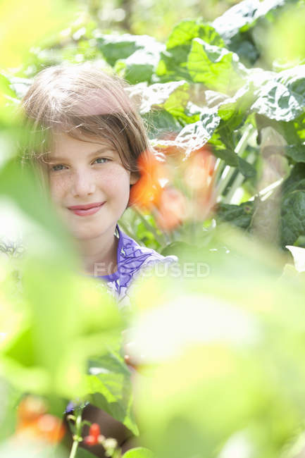 Pre-teen girl sitting among fresh green foliage of garden. — Stock Photo