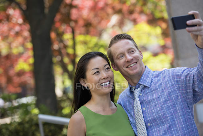 Couple taking selfie with smartphone in autumnal city park. — Stock Photo