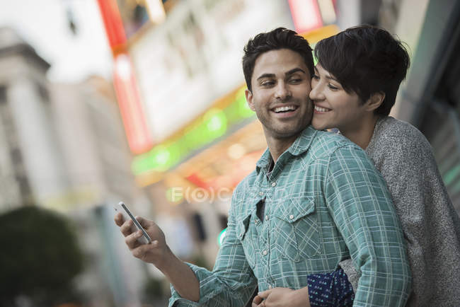 Homem e mulher abraçando na rua da cidade enquanto segurando smartphone . — Fotografia de Stock