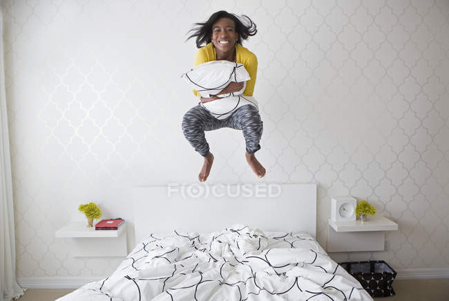 Teenage girl jumping in mid air above bed while holding blanket. — Stock Photo